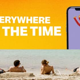 people relaxing on beach while a gian iphone floats out of the water with an air tube dancer advertising to them