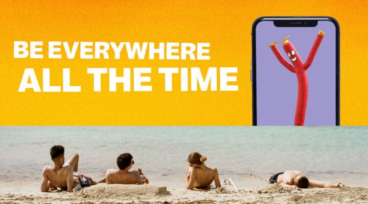 people relaxing on beach while a gian iphone floats out of the water with an air tube dancer advertising to them
